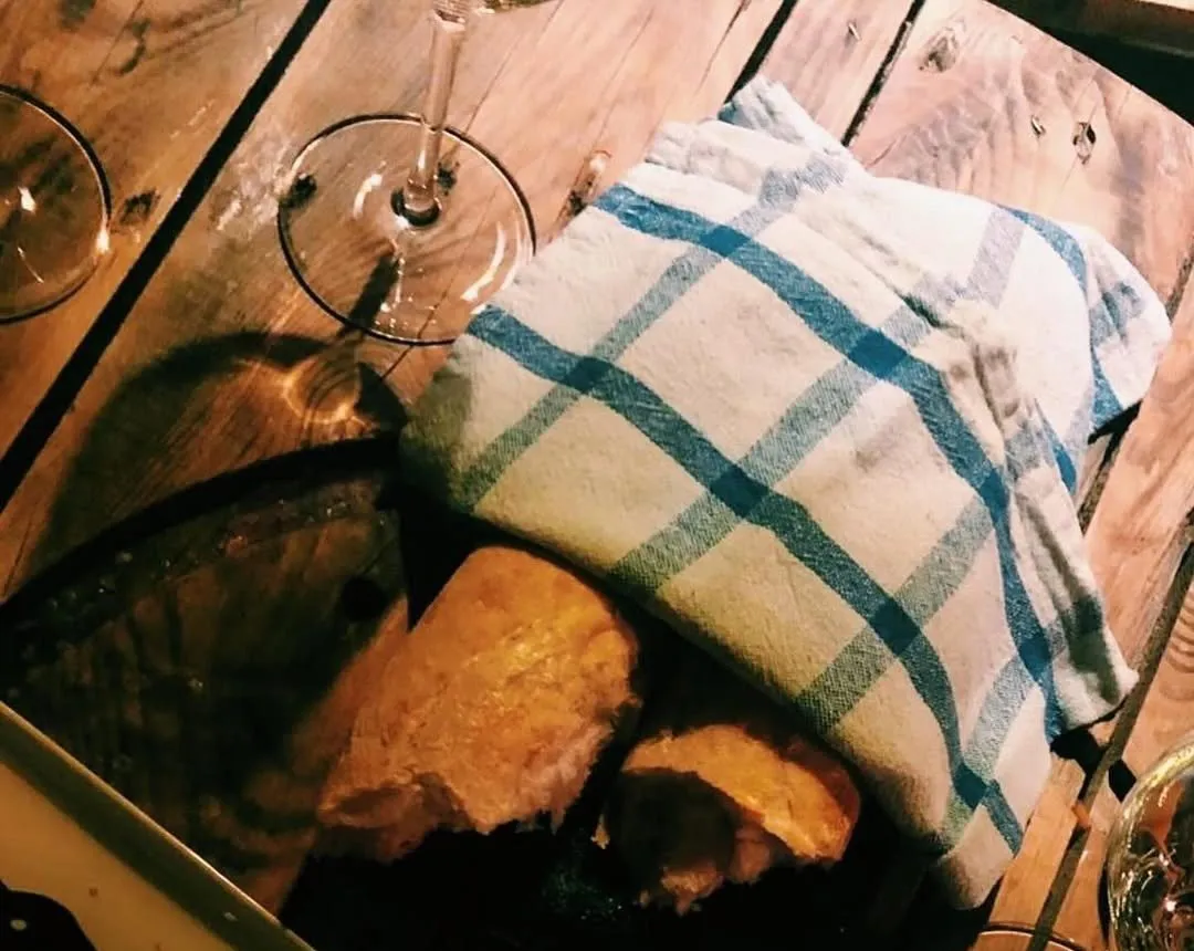 Vīna glāzes un maize zem rūtaina dvieļa uz koka galda